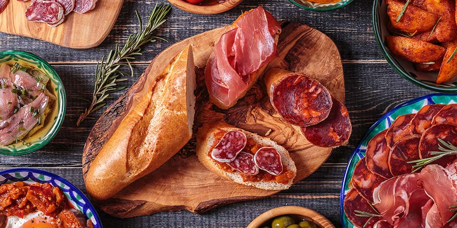 A table full of traditional Spanish tapas: green olives, cured meats, and vibrant vegetable dishes. 